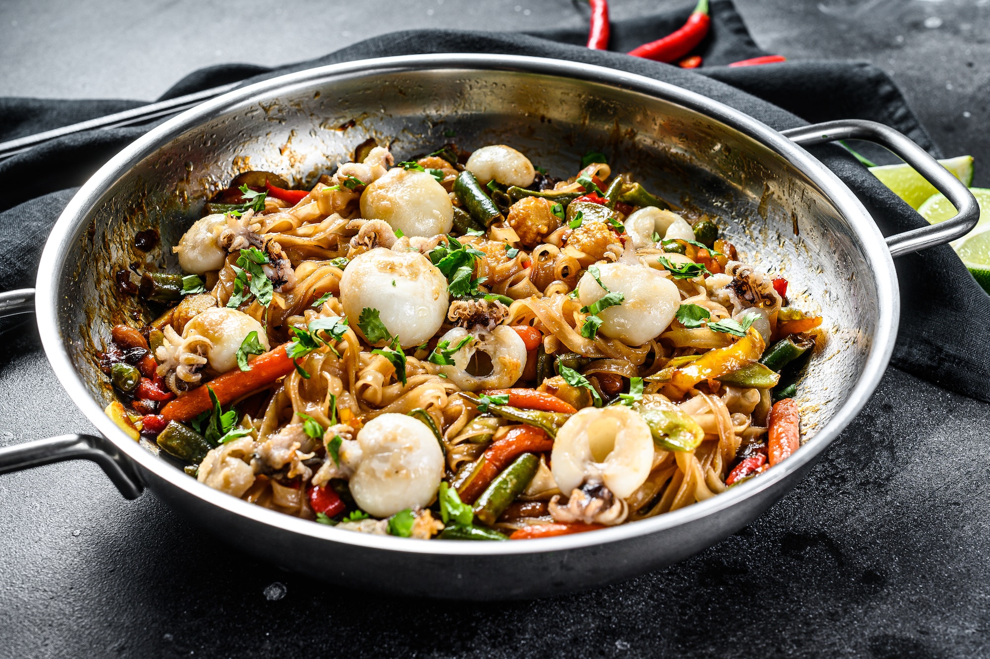 Stir fry noodles with seafood and vegetables in a wok pan. Black background. Top view